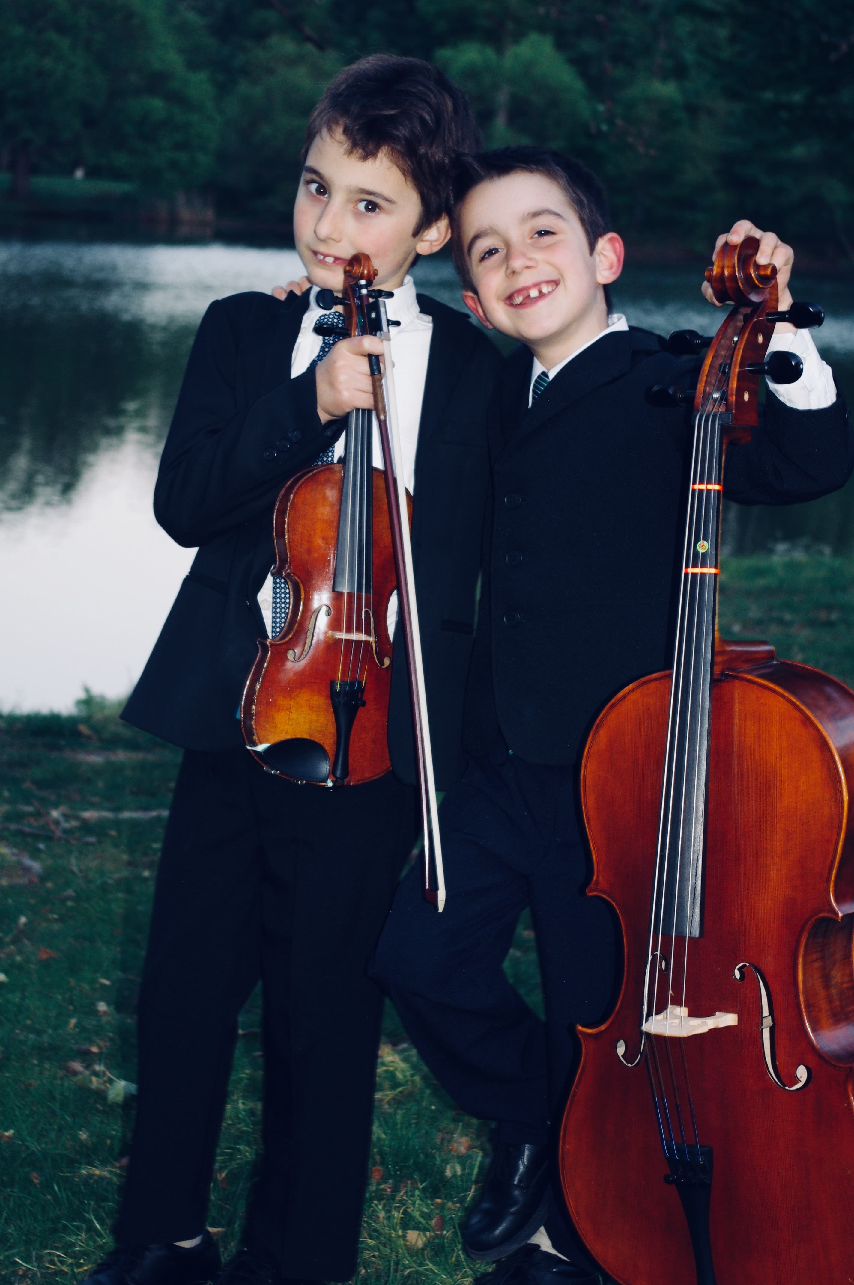 Two young students holding a violin and cello by a lake at dusk