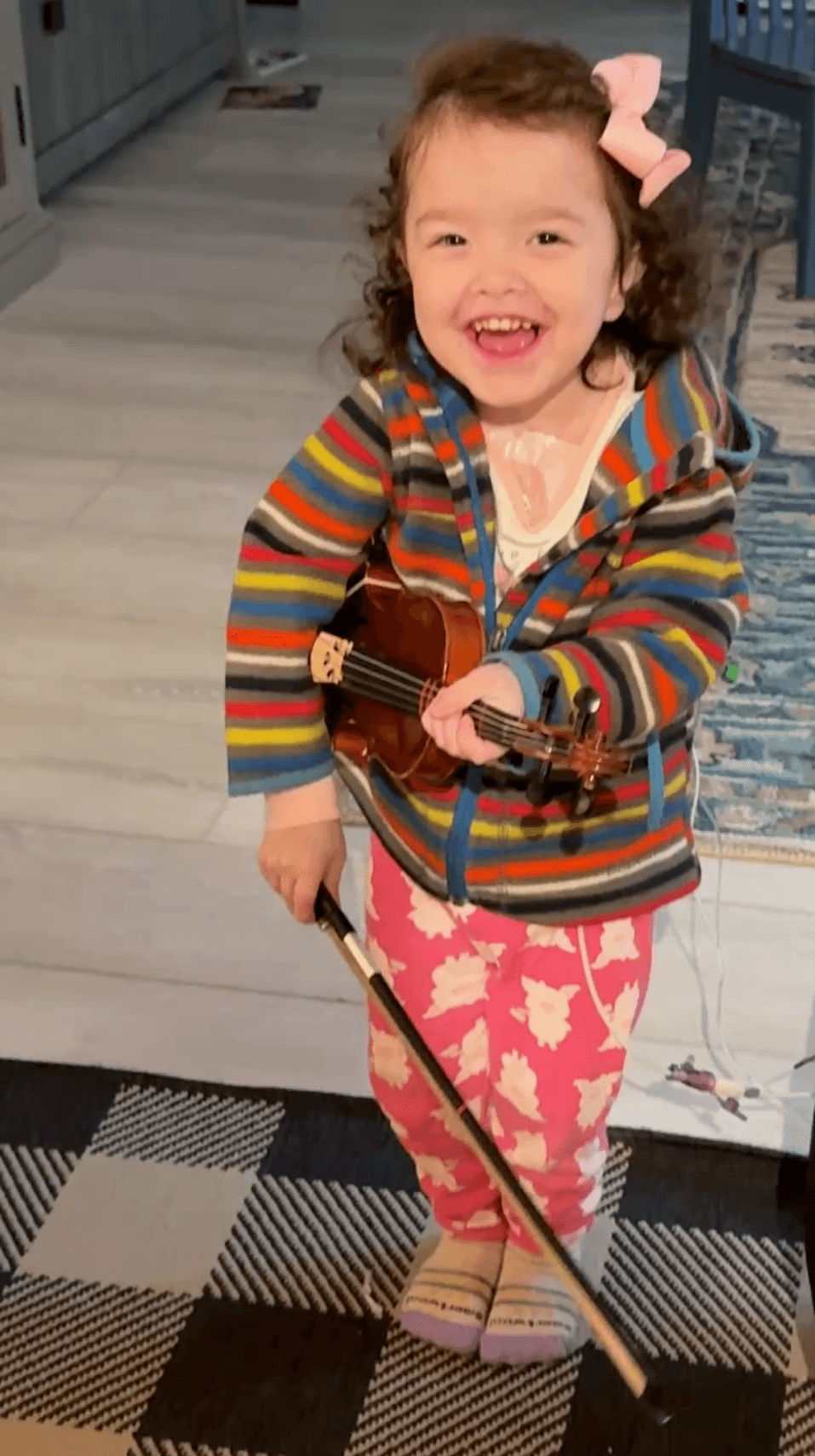 A laughing toddler cradling a small violin and bow