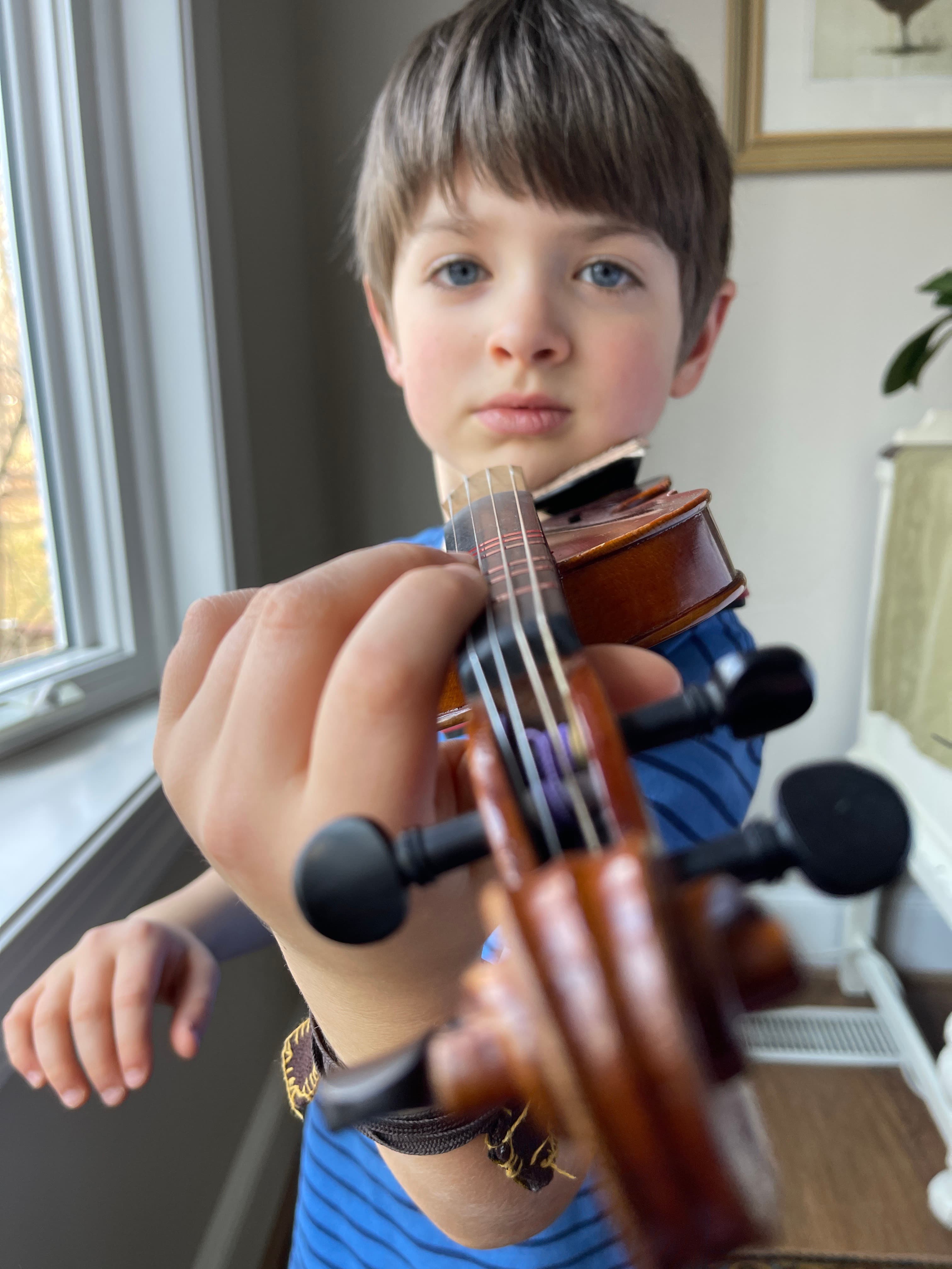 A boy tuning his violin in a sunlit room